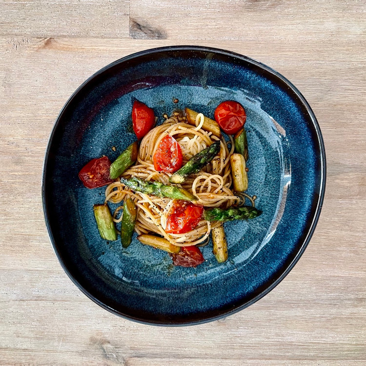Blauer Teller mit Gericht: Spaghetti mit grünem Spargel und Kirschtomatenten